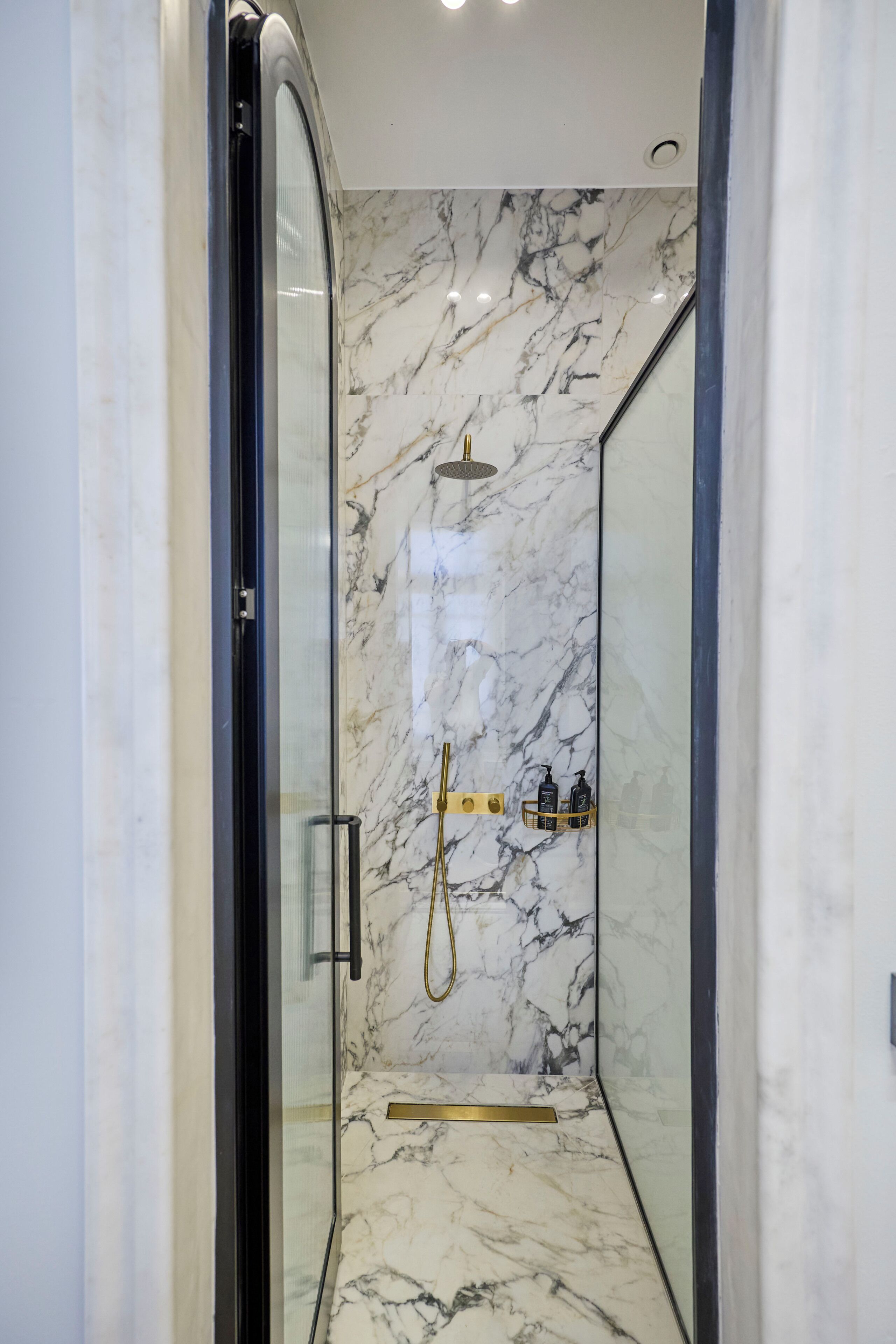 A modern bathroom with a glass-enclosed shower, marble walls, and a gold showerhead.