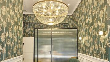 A room with patterned wallpaper, a chandelier, two green armchairs, a small table, and a door with a frosted glass panel.