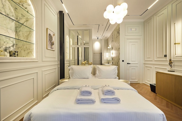 A hotel room with a large bed, two bedside tables, a mirror, and a chandelier.
