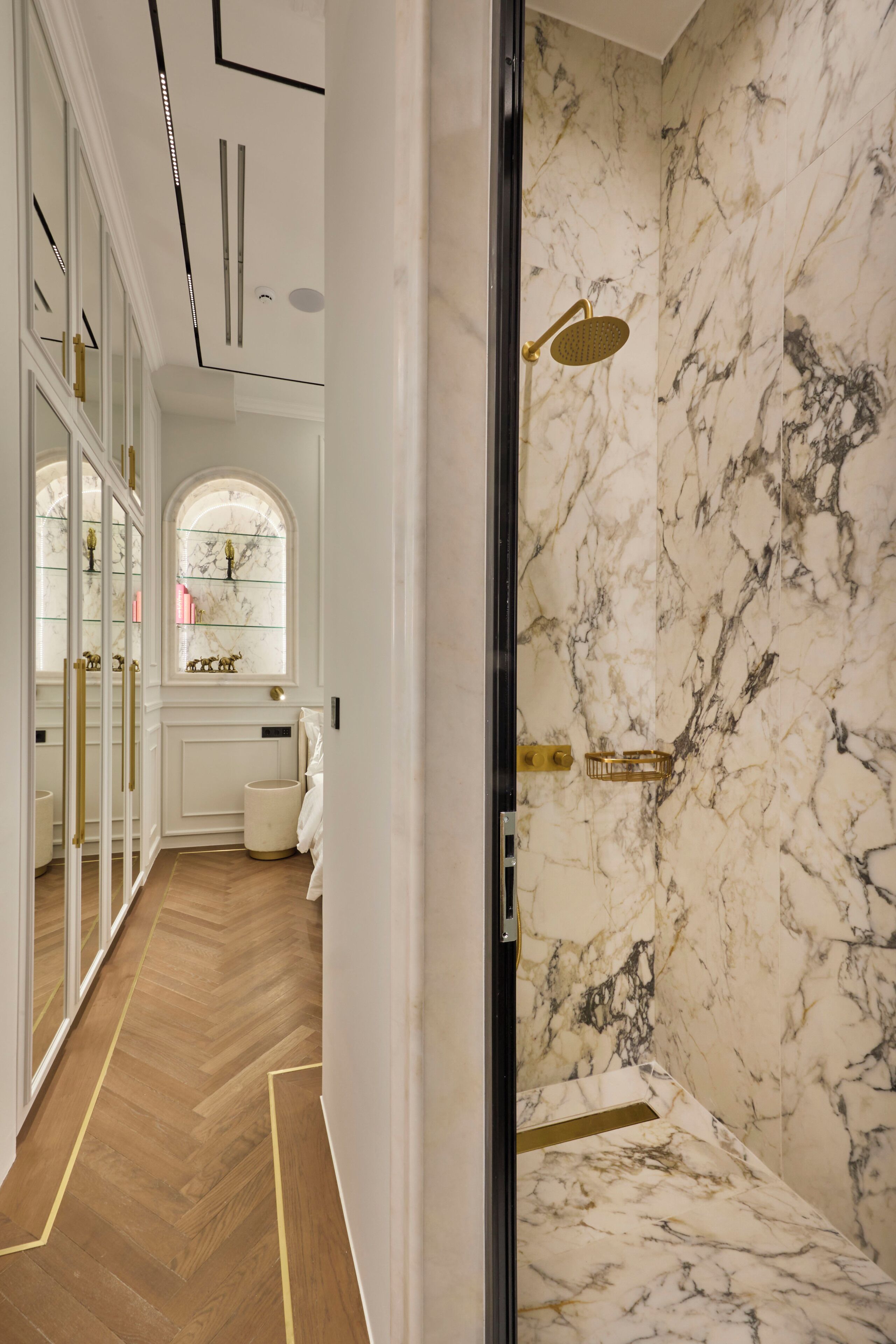 A bathroom with marble walls, a shower with a gold showerhead, and a wooden floor.