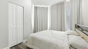 Un dormitorio con cama, armario y ventana con cortinas.