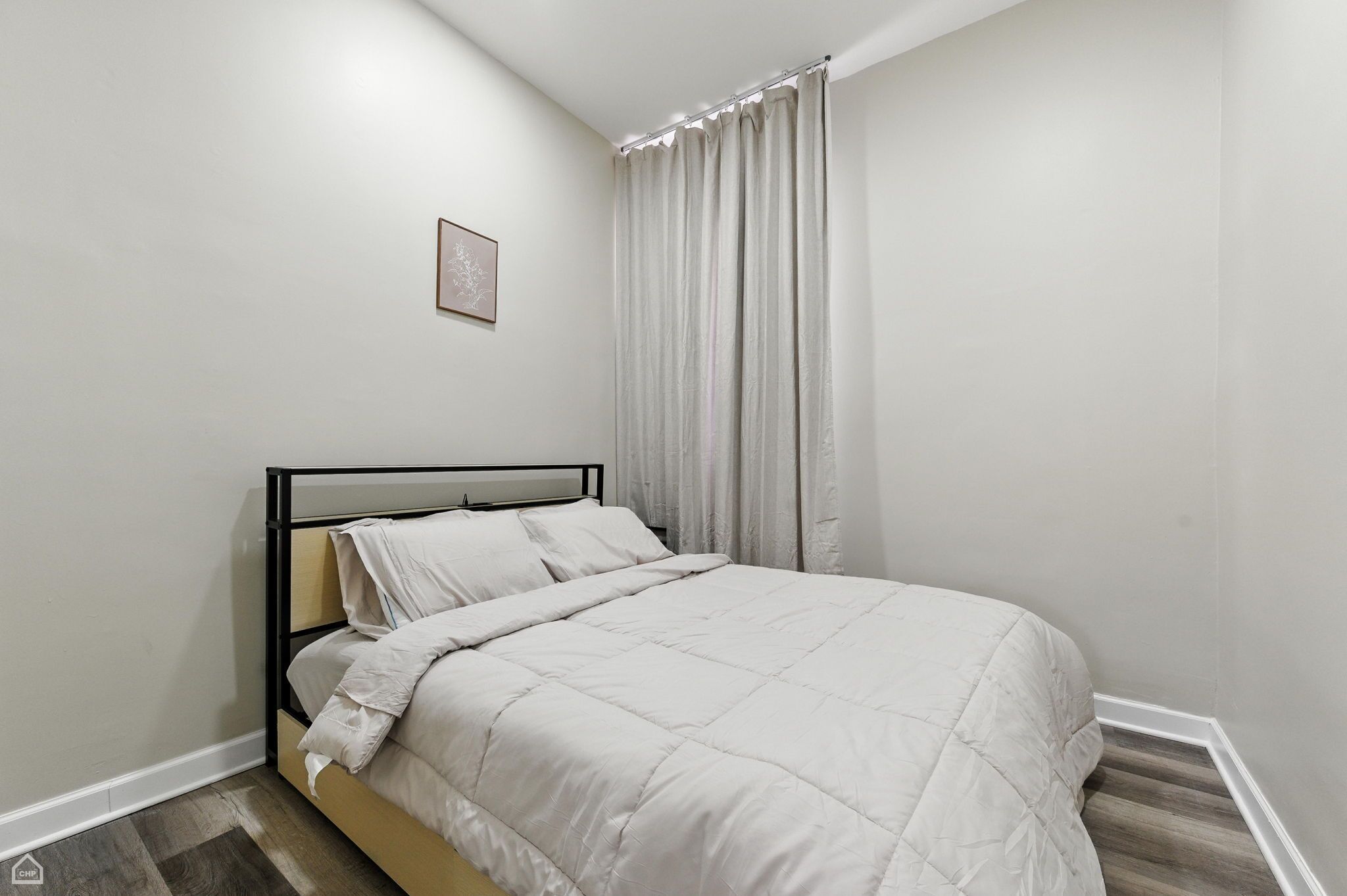 Ein Schlafzimmer mit einem Bett, weißen Vorhängen und einem gerahmten Bild an der Wand.