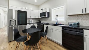 Una cocina moderna con armarios blancos, un refrigerador de acero inoxidable, un microondas, una estufa y un lavavajillas.
