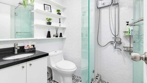 Een moderne badkamer met een douche met glazen wand, witte tegels, een zwart aanrecht en een toilet.