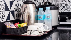 Een aanrecht met een waterkoker, twee waterflessen, een koffiezetapparaat, een dienblad met snacks, en een beker.
