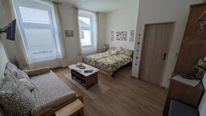 Een knus kamertje met een bed, een bank, een houten salontafel en een deur.