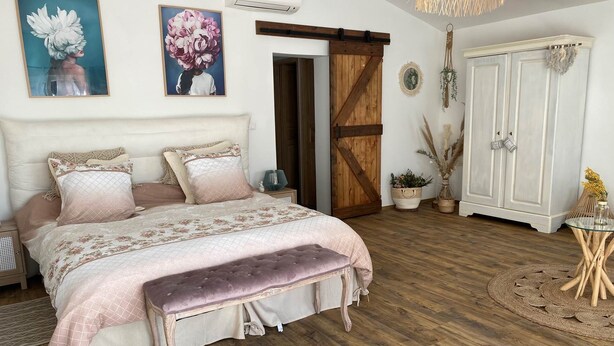 Un dormitorio con una cama grande, suelo de madera, un armario y una lámpara colgante.