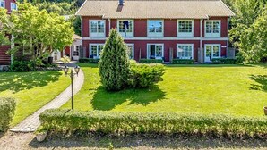 A two-story building with a red facade and white trim, surrounded by a well-maintained lawn and a pathway leading to the entrance. - 2 Person Holiday Park Home in Bastad (Bastad)