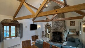 Un loft espacioso con vigas de madera a la vista, una chimenea de piedra, un comedor con mesa y sillas de madera, y un rincón de descanso acogedor con un sofá azul.