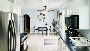 Une cuisine moderne dotée d’appareils électroménagers en acier inoxydable, un coin repas avec une table et des chaises, et un ventilateur de plafond.