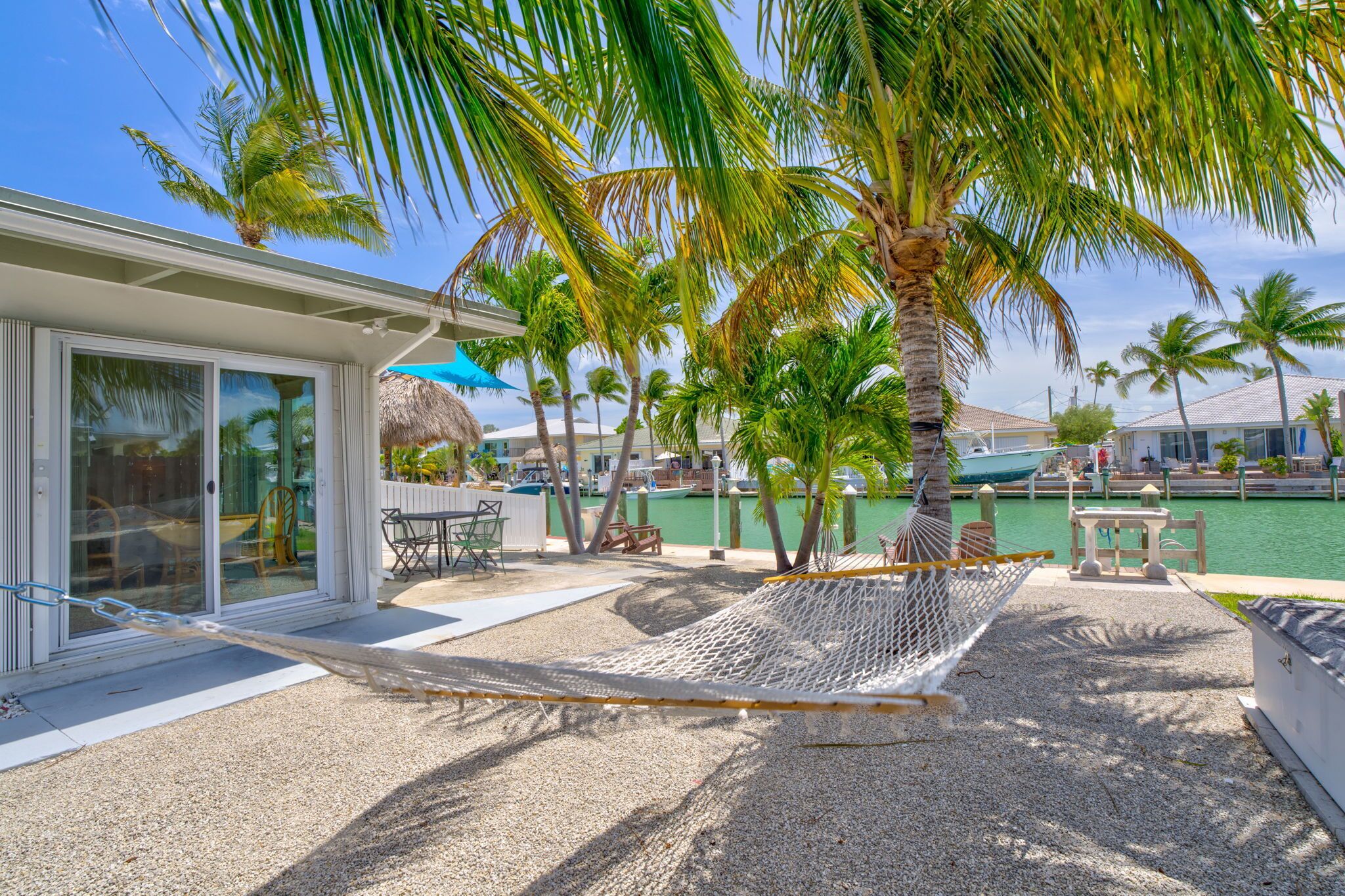 Une terrasse au bord de la plage, avec un hamac, des palmiers, une piscine et une maison dotée de grandes fenêtres.