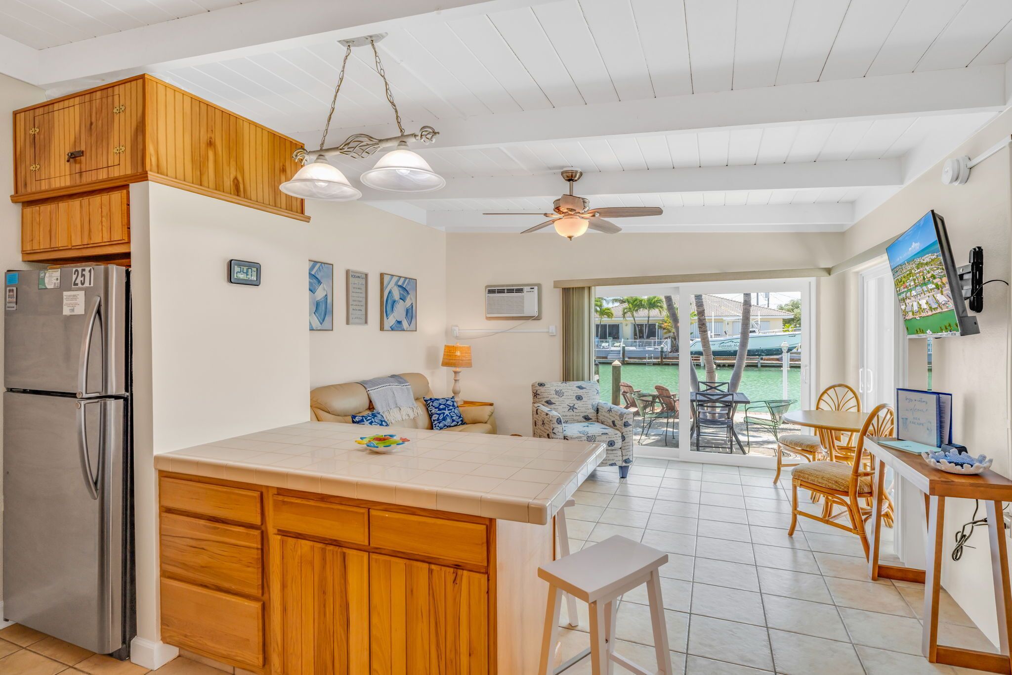 A kitchen with wooden cabinets, a stainless steel refrigerator, a central island, and a dining area with wicker chairs and a table.