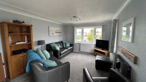 A living room with a sofa, a television, a wooden cabinet, and a window with a view of the outside.