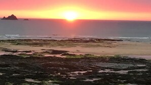 A sunset over a rocky beach with calm waves.