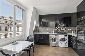 A modern kitchen with built-in appliances, a dining area with a table and chairs, and a large window offering a view of the cityscape. - Cozy 2BR Near Parc Monceau & Opera (Paris)