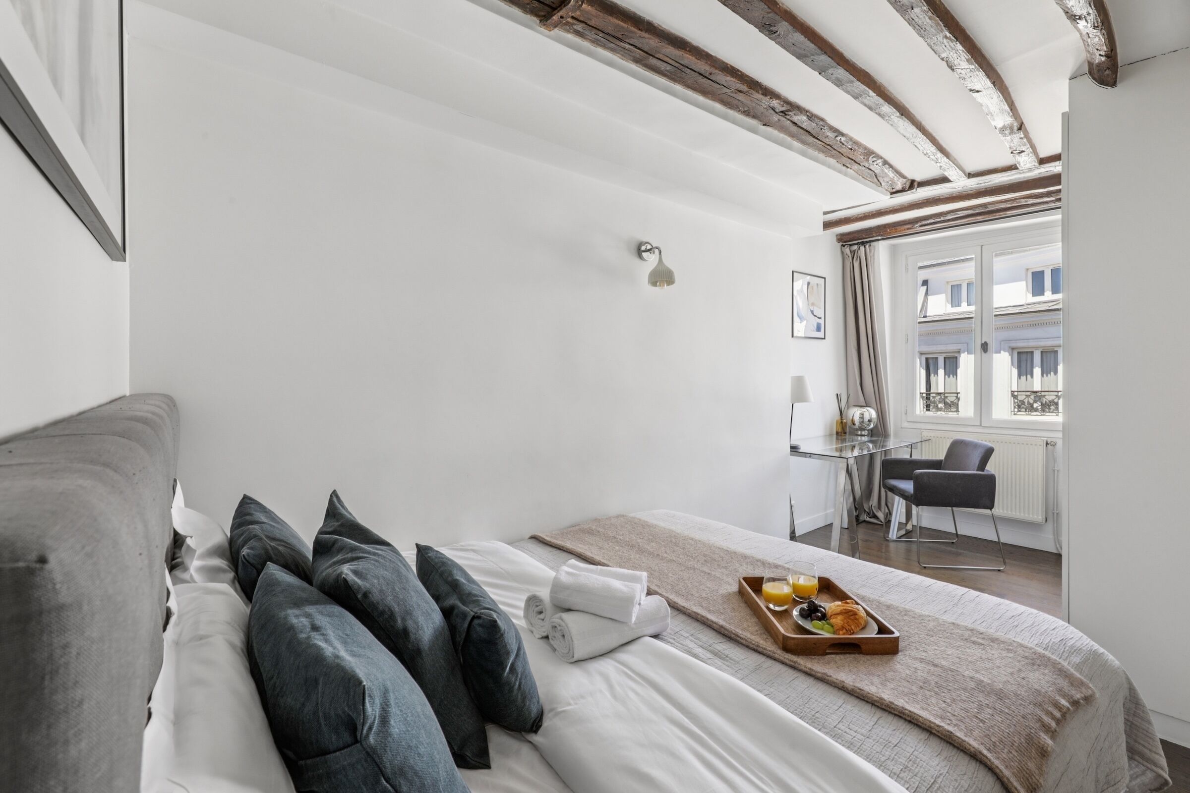 Une chambre d’hôtel moderne avec un grand lit, une petite table où le petit-déjeuner est servi, et une vue sur la ville par la fenêtre.