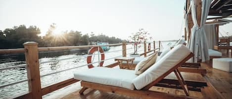 A wooden deck with a lounge chair and a life buoy, overlooking a body of water.
