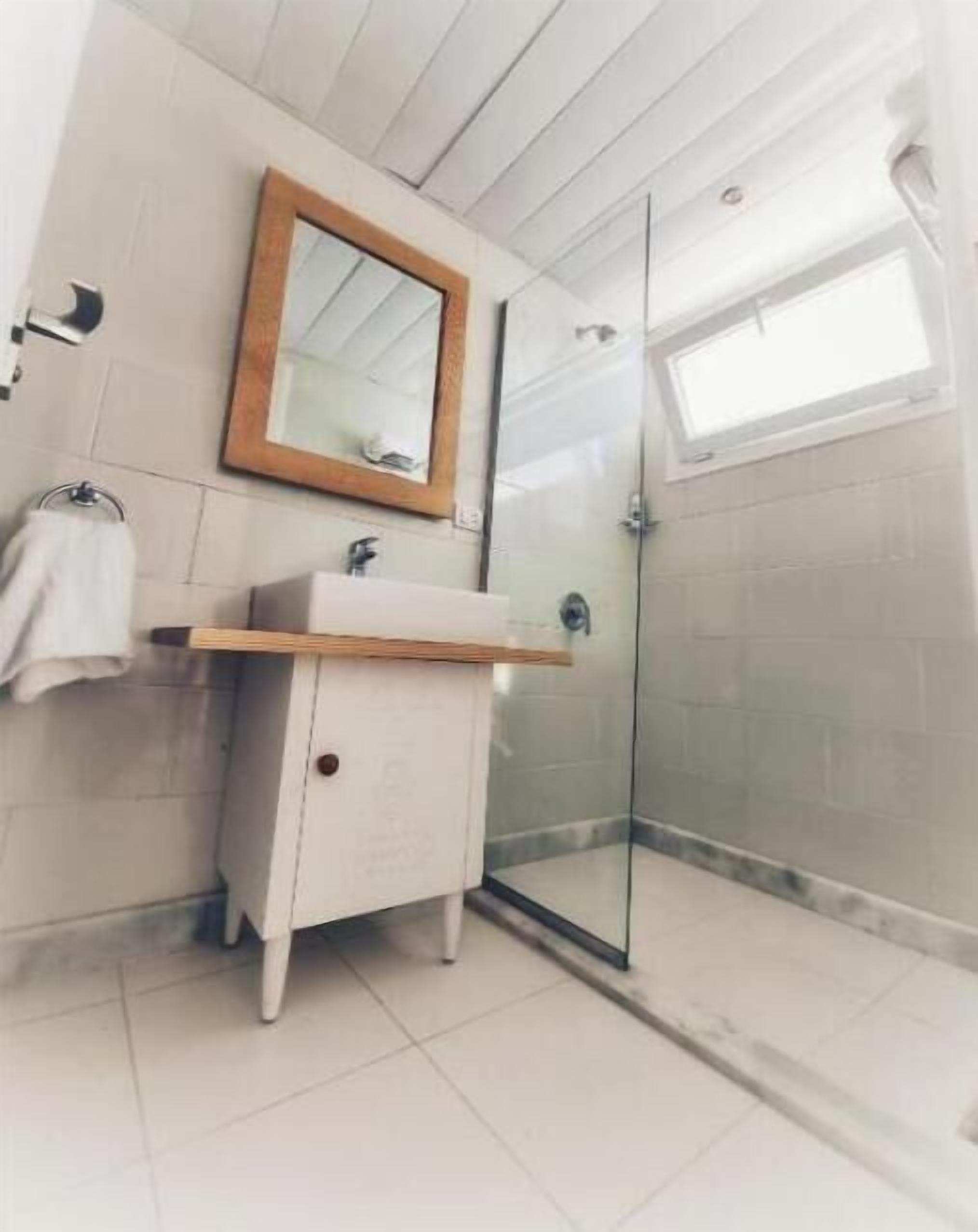 A modern bathroom with a glass shower enclosure, a wooden-framed mirror, and a white vanity with a sink.