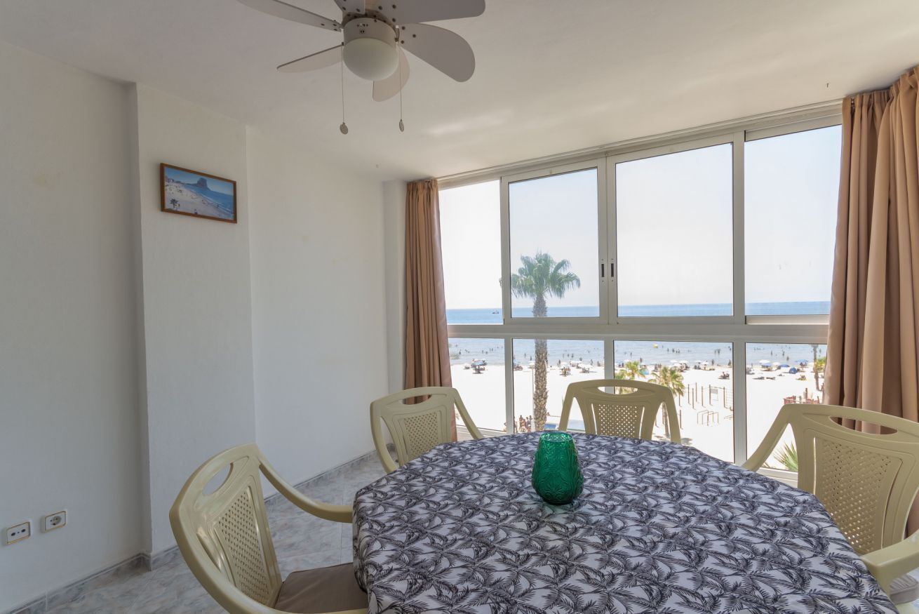 Ein Zimmer mit großem Fenster mit Blick auf einen Strand, einem Deckenventilator und einem Tisch mit Stühlen.
