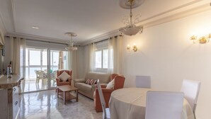 A spacious living room with a dining area, large windows, and a chandelier. - Apartamento Joya 3 by Costa CarpeDiem (Calpe)