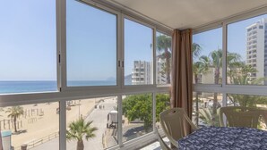 A balcony with a bed, large windows, and a view of the beach and buildings. - Apartamento Joya 3 by Costa CarpeDiem (Calpe)