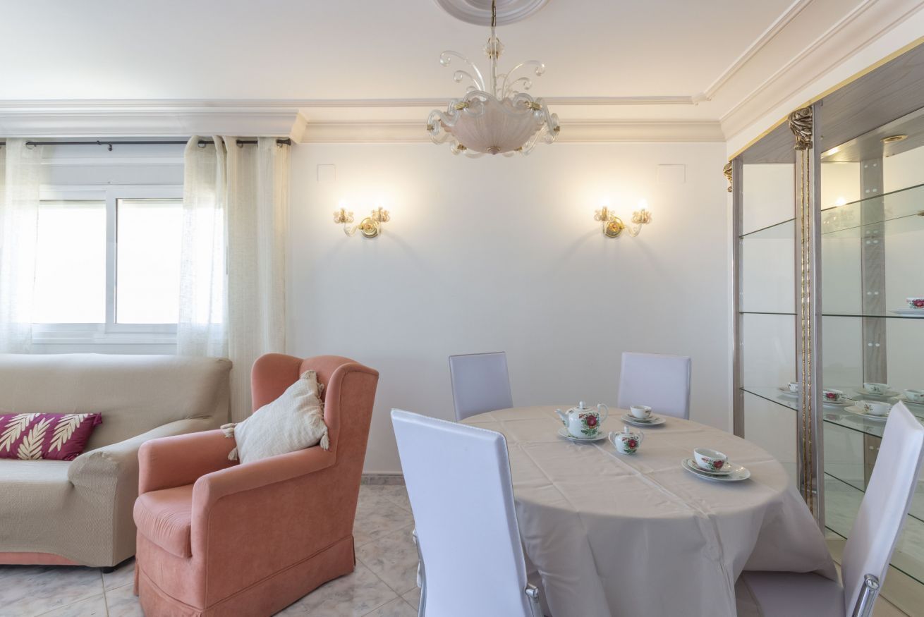 Een eetgedeelte met een ronde tafel, witte stoelen en een kroonluchter.