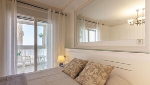 A bedroom with a bed, a nightstand, a lamp, a large mirror, and a view of an outdoor balcony. - Apartamento Joya 3 by Costa CarpeDiem (Calpe)