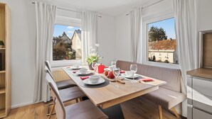 Zona pranzo con tavolo di legno apparecchiato per quattro persone, panche e vista su una zona residenziale tramite ampie finestre.