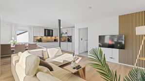 Un soggiorno moderno con divano, tavolino e televisione. Sullo sfondo, una cucina con mobili bianchi e un'area pranzo con tavolo e sedie.