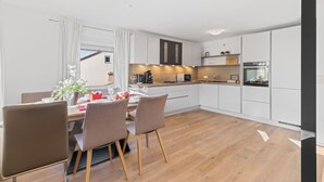 Una cucina moderna con mobili bianchi, un piano di lavoro in legno e un forno a incasso. C'è una zona pranzo con tavolo e sedie, e una finestra con tende.