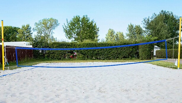Un terrain de volley-ball avec un filet, entouré de sable et de verdure.