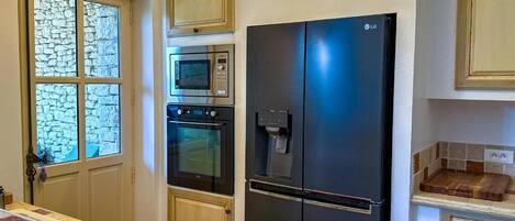 A kitchen with a black refrigerator, an oven, a microwave, and a stone-framed window.
