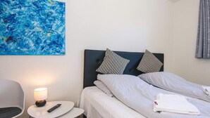 A hotel room with a bed, a small table with a lamp, a chair, and a painting on the wall.