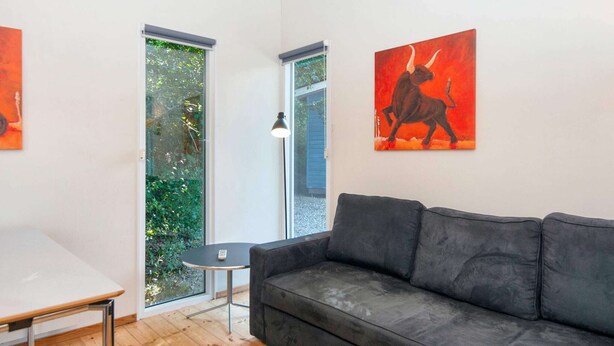 A modern living room with a grey sofa, a small round table, and a window with a view of greenery.