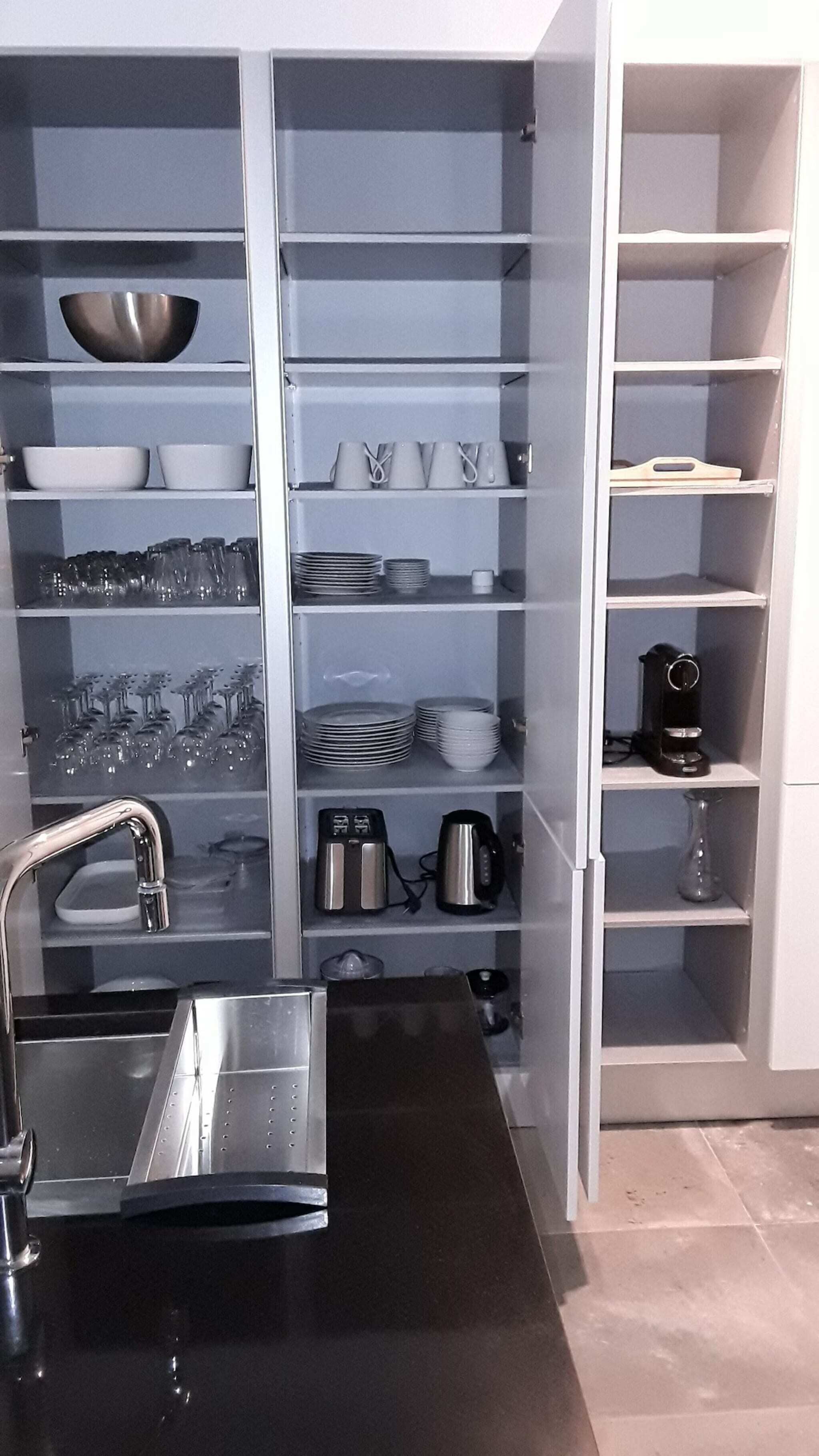 Una cocina moderna con electrodomésticos de acero inoxidable, un lavaplatos empotrado y estantes organizados para platos y vasos.