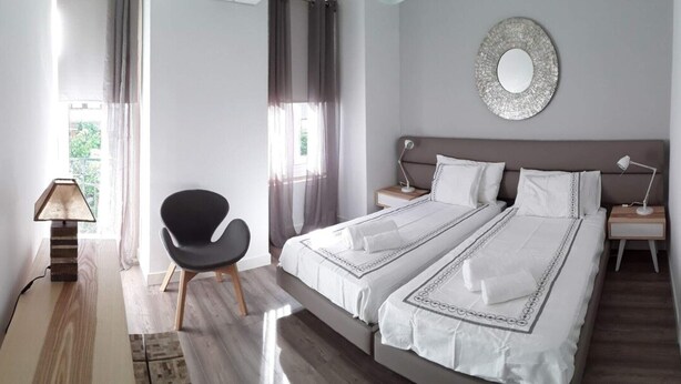 A modern bedroom with a large bed, a chair, a bedside table with a lamp, and a decorative mirror on the wall.