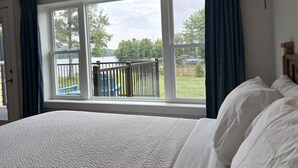 Quarto com cama grande, janela com cortinas e vista para uma varanda e vegetação lá fora.