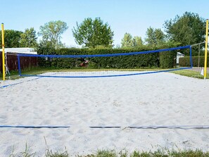 Ein Volleyballfeld mit Netz, umgeben von Sand und Grün.