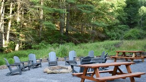 A gravel area with Adirondack chairs and picnic tables, surrounded by dense forest.