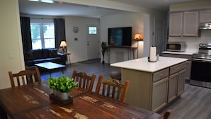 A modern kitchen with a dining area, wooden furniture, and a flat-screen TV.