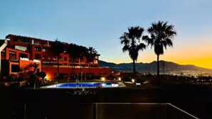 A hotel with a pool, palm trees, and a mountain in the background.