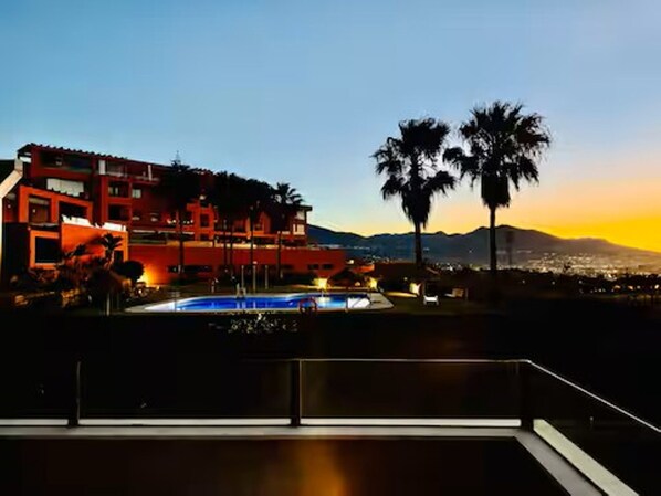 A hotel with a pool, palm trees, and a mountain in the background.