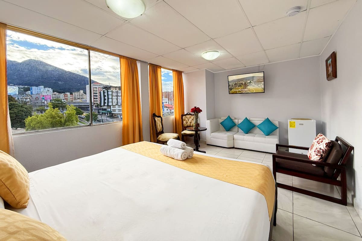 Habitación de hotel con cama, sofá, sillón, mesa y vista panorámica de la ciudad.