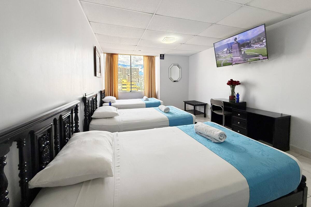 Habitación de hotel con dos camas, un escritorio, una silla, un televisor y una ventana con vistas a la ciudad.