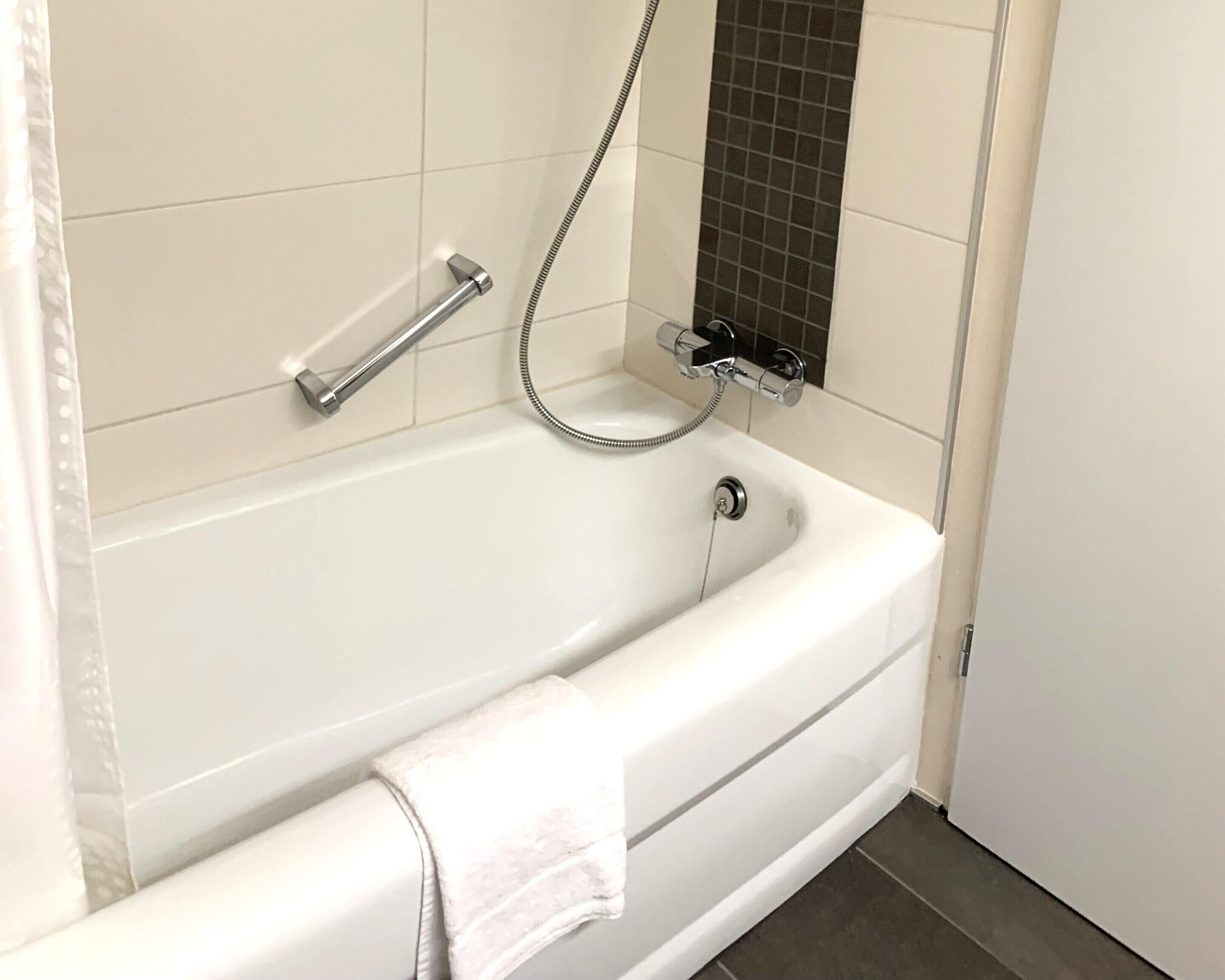 Une salle de bain moderne avec une baignoire blanche, une douchette à main et une serviette sur le sol.