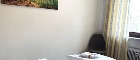 A hotel room with two beds, each with neatly folded white towels and pillows. A large forest painting is hung on the wall above the beds.