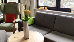 A living room with a grey sofa, a wooden coffee table with a vase of yellow flowers, and a chair with a red cushion. - Winterberg Apartment 21041 (Winterberg)