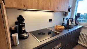A modern kitchen with a built-in stove, coffee maker, and a window providing a view of the outdoors. - Apartment in the Centre of Winterberg (Winterberg)