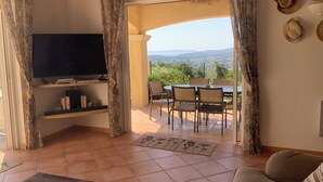 A living room with a TV, a sofa, and a dining area with chairs and a table. - MAGNIFICENT VILLA SEA VIEW 4 BEDROOMS SWIMMING POOL QUIET ON THE HEIGHTS OF BORMES (Bormes-les-Mimosas)