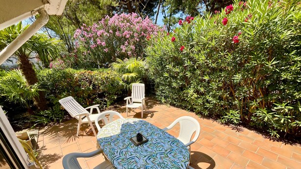 An outdoor patio with a table and chairs, surrounded by lush greenery and flowering plants.